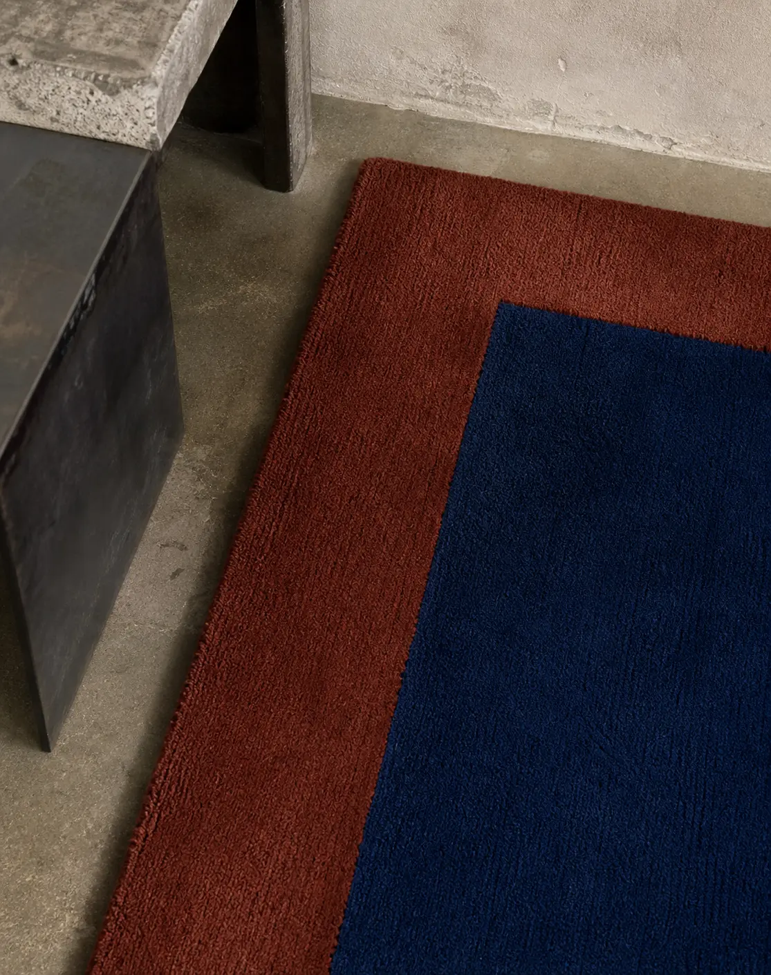 Close-up of Thick rug in Lapis and Brick beside stone furniture.